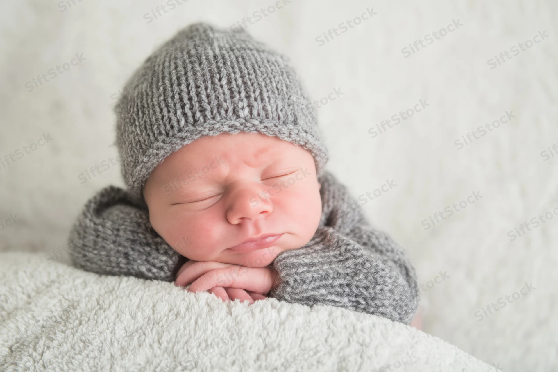 Newborn baby sleeping peacefully in gray knitted hat and sweater on white textured blanket