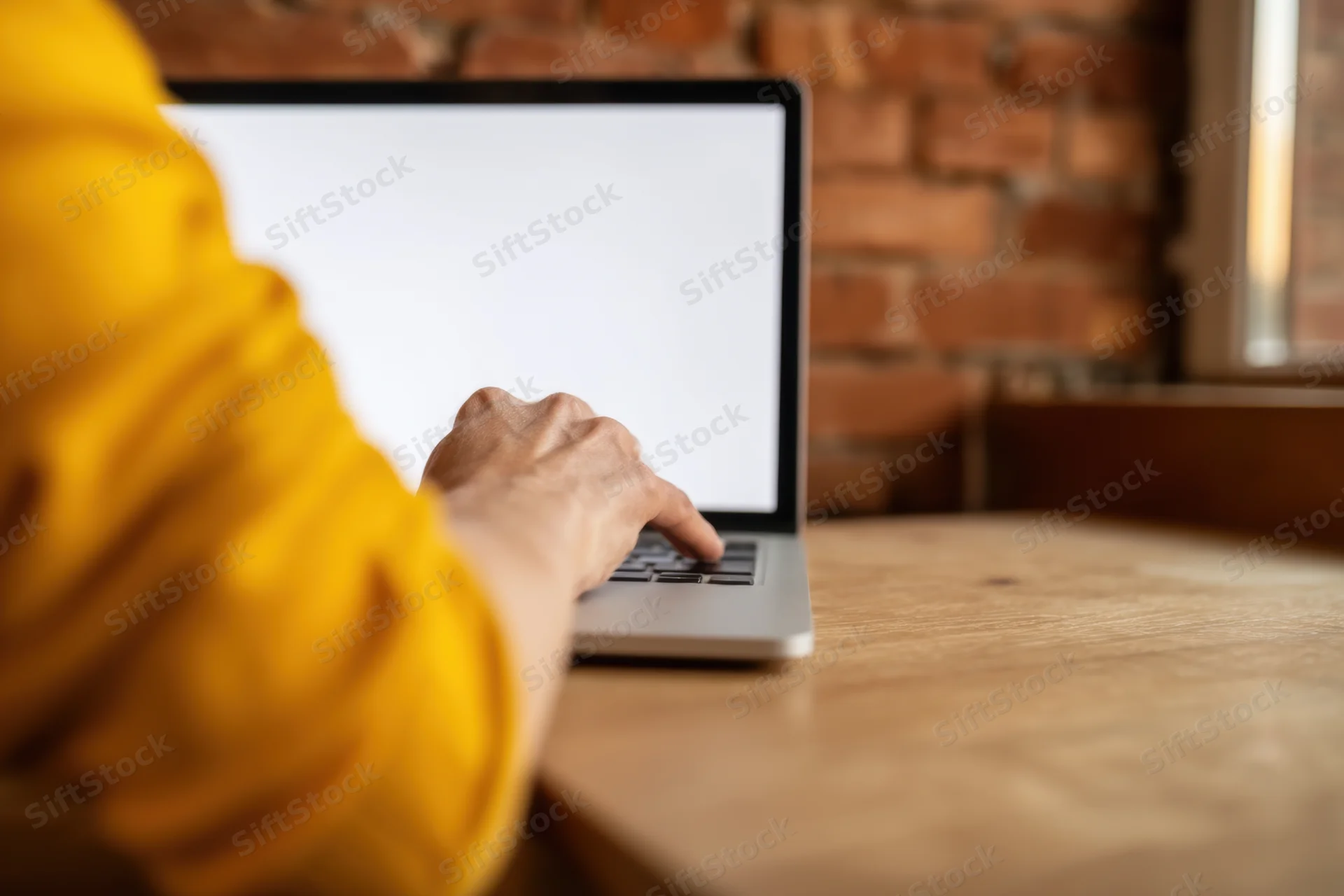 Person typing on laptop at wooden desk with brick wall background