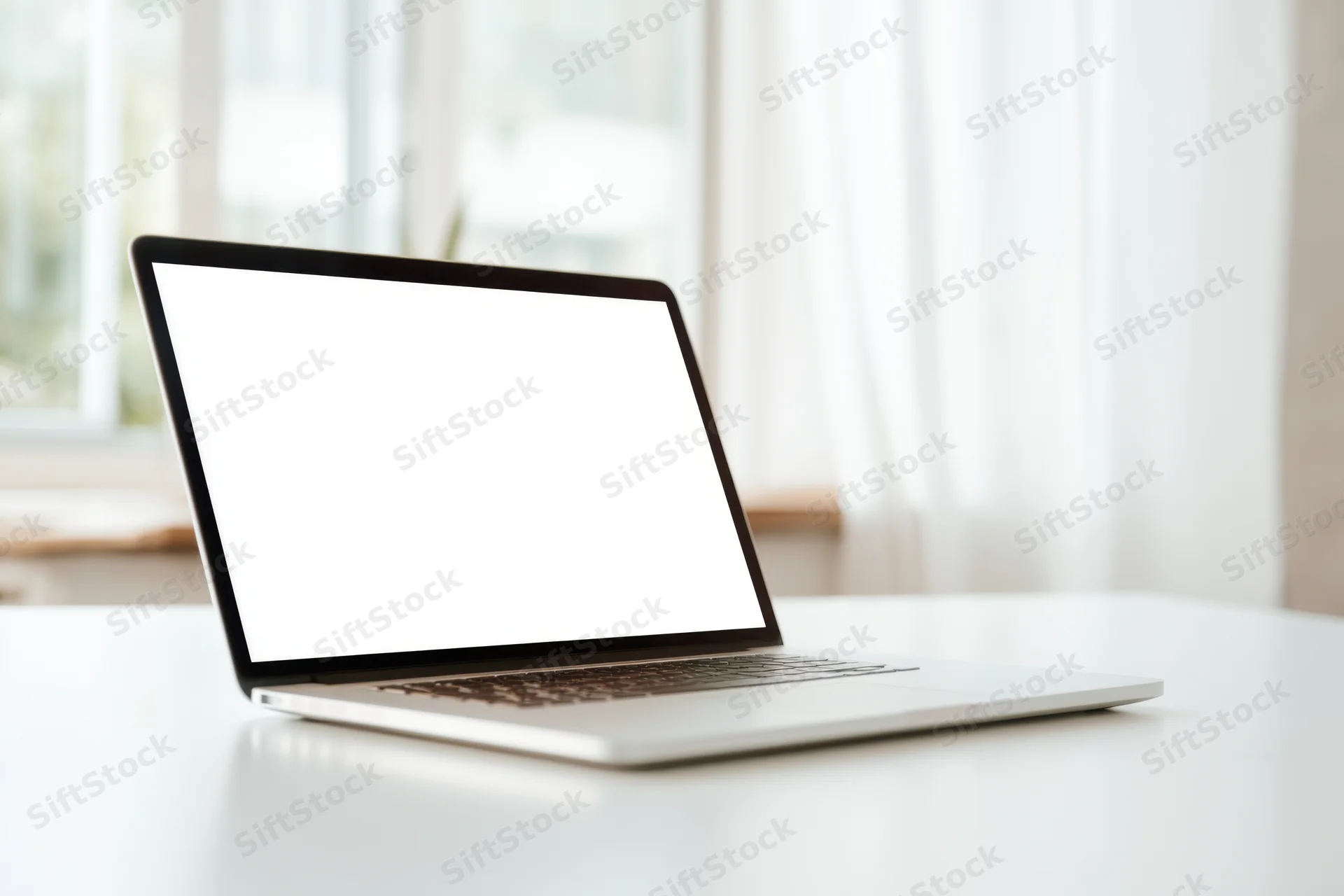 Sleek laptop with blank white screen on white desk near window