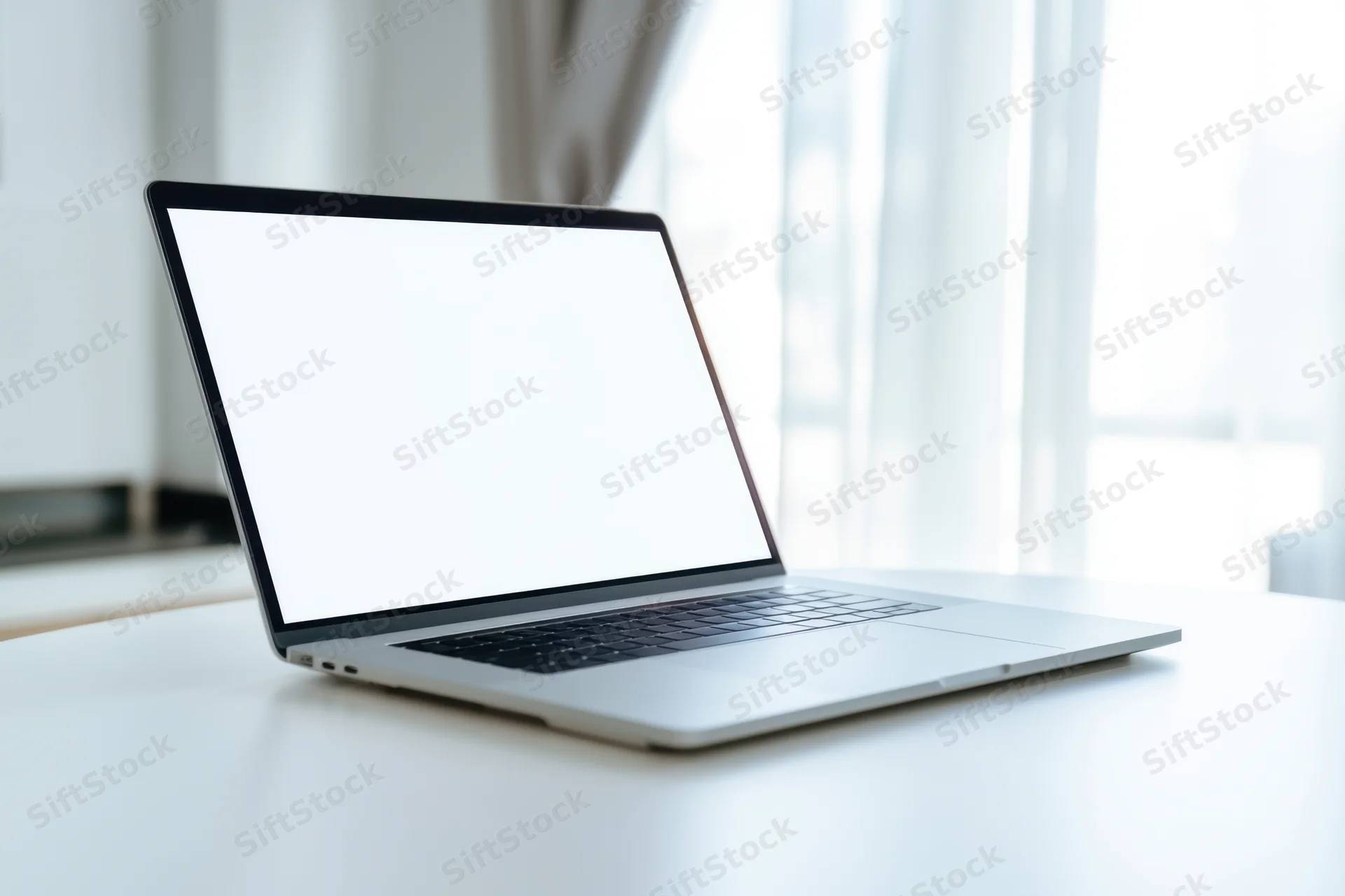 Sleek silver laptop with blank white screen on white desk near window