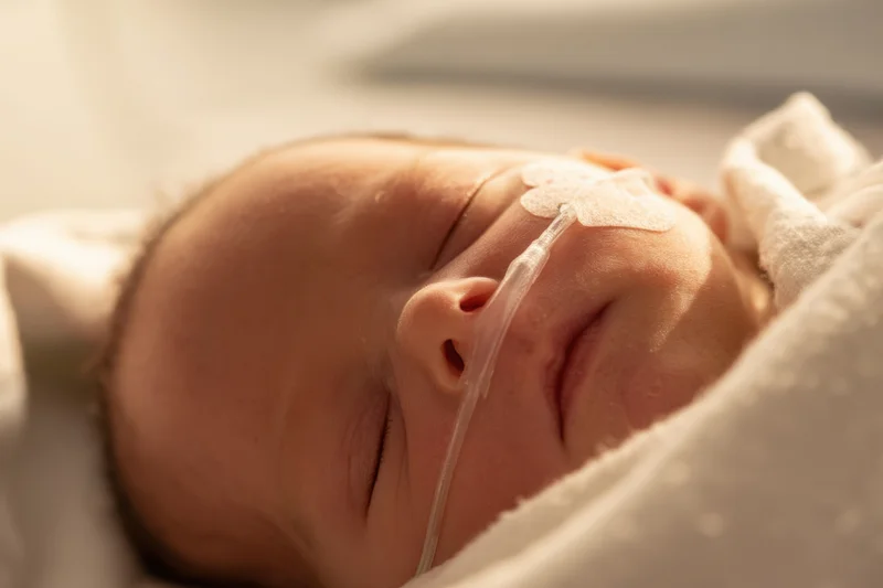 Sleeping newborn with nasal oxygen tube on face wrapped in white blanket