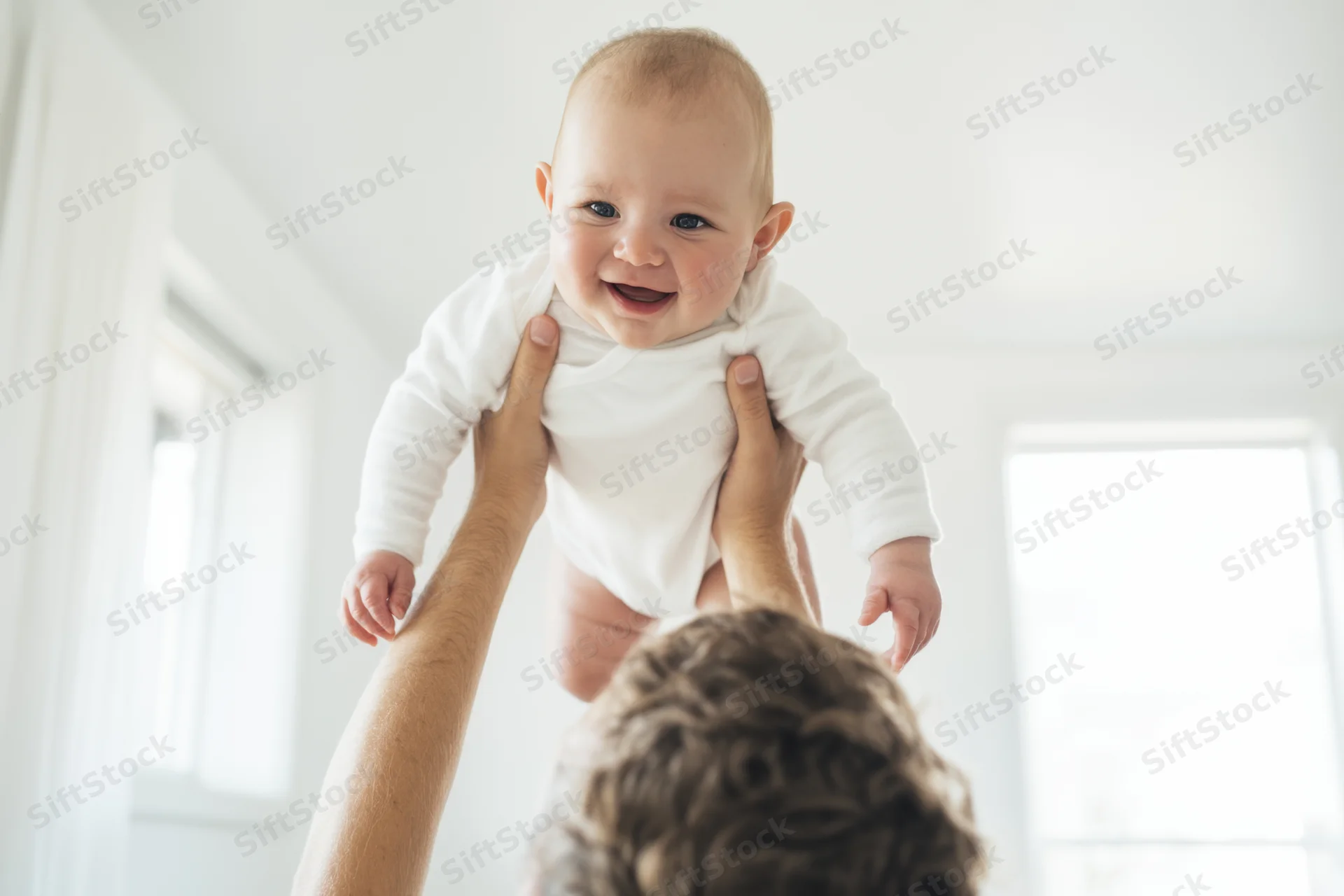 Smiling baby being lifted in the air by a parent indoors