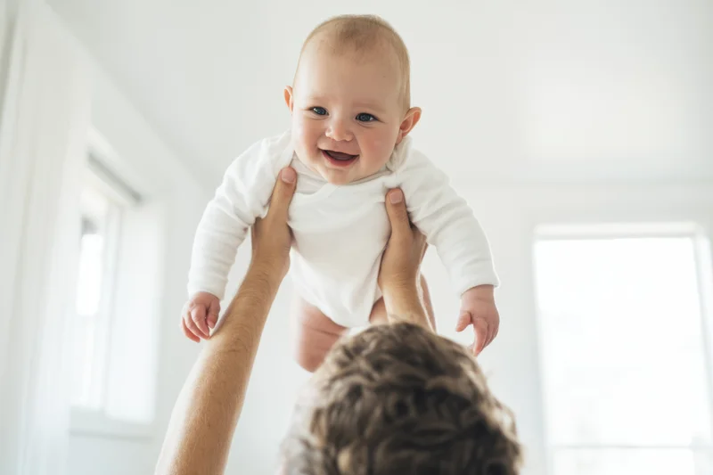 Smiling baby being lifted in the air by a parent indoors