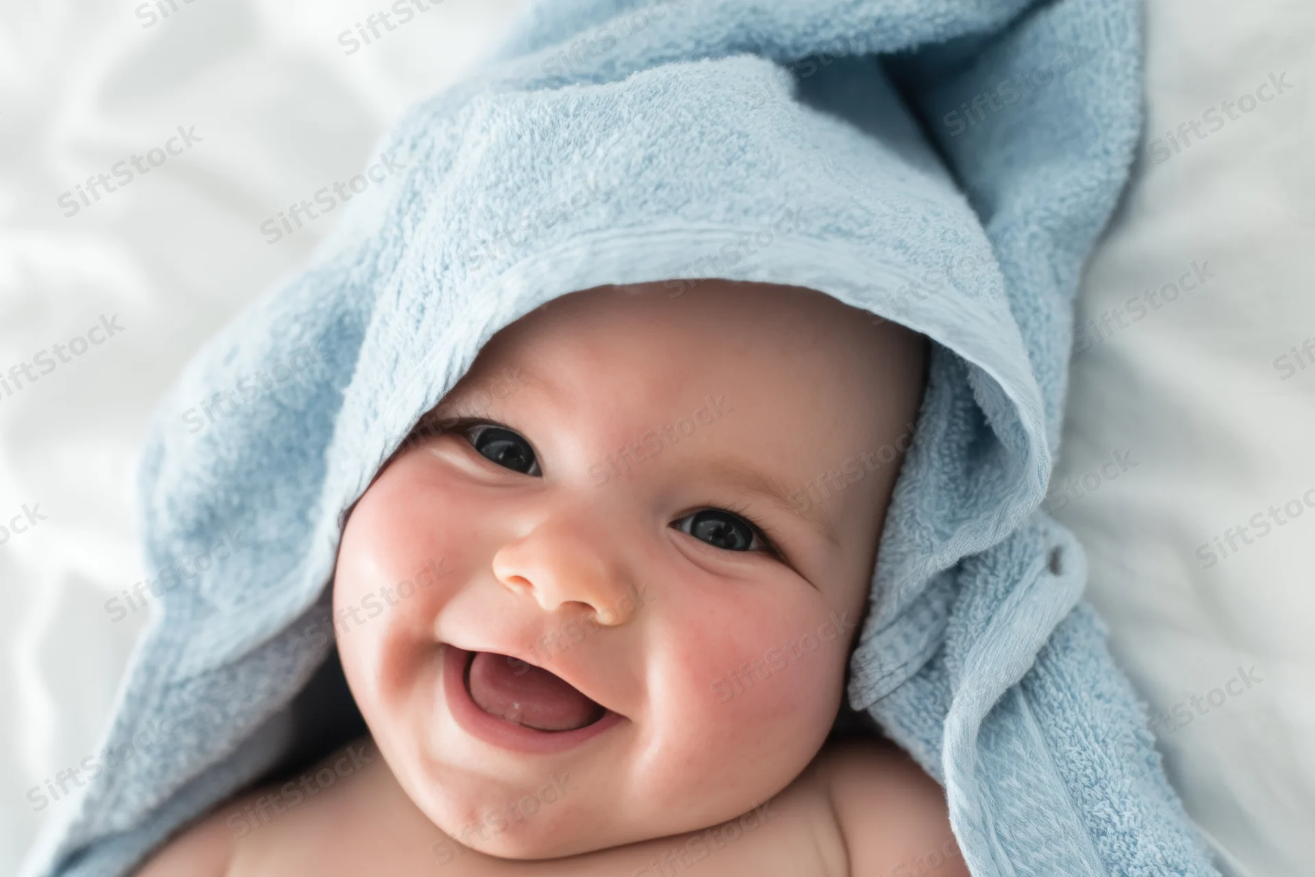 Smiling baby wrapped in blue towel lying on white bed