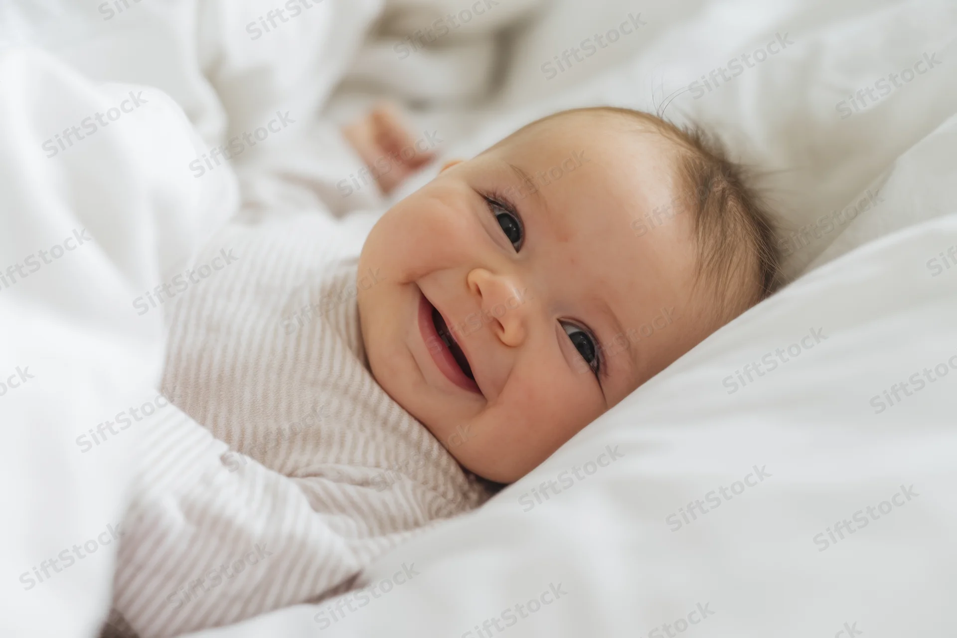 Smiling baby lying on white bed wearing striped onesie