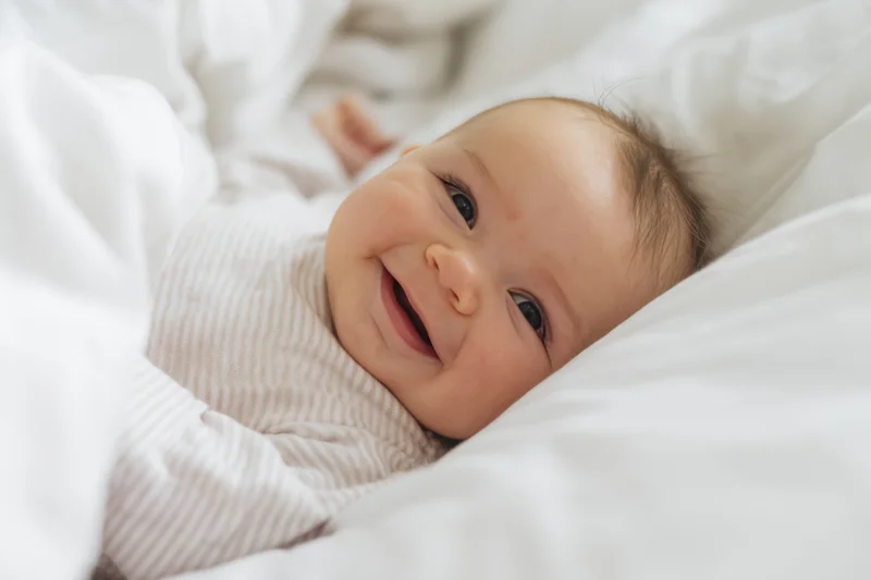 Smiling baby lying on white bed wearing striped onesie