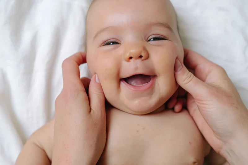 Smiling baby being gently held by hands on a soft white surface