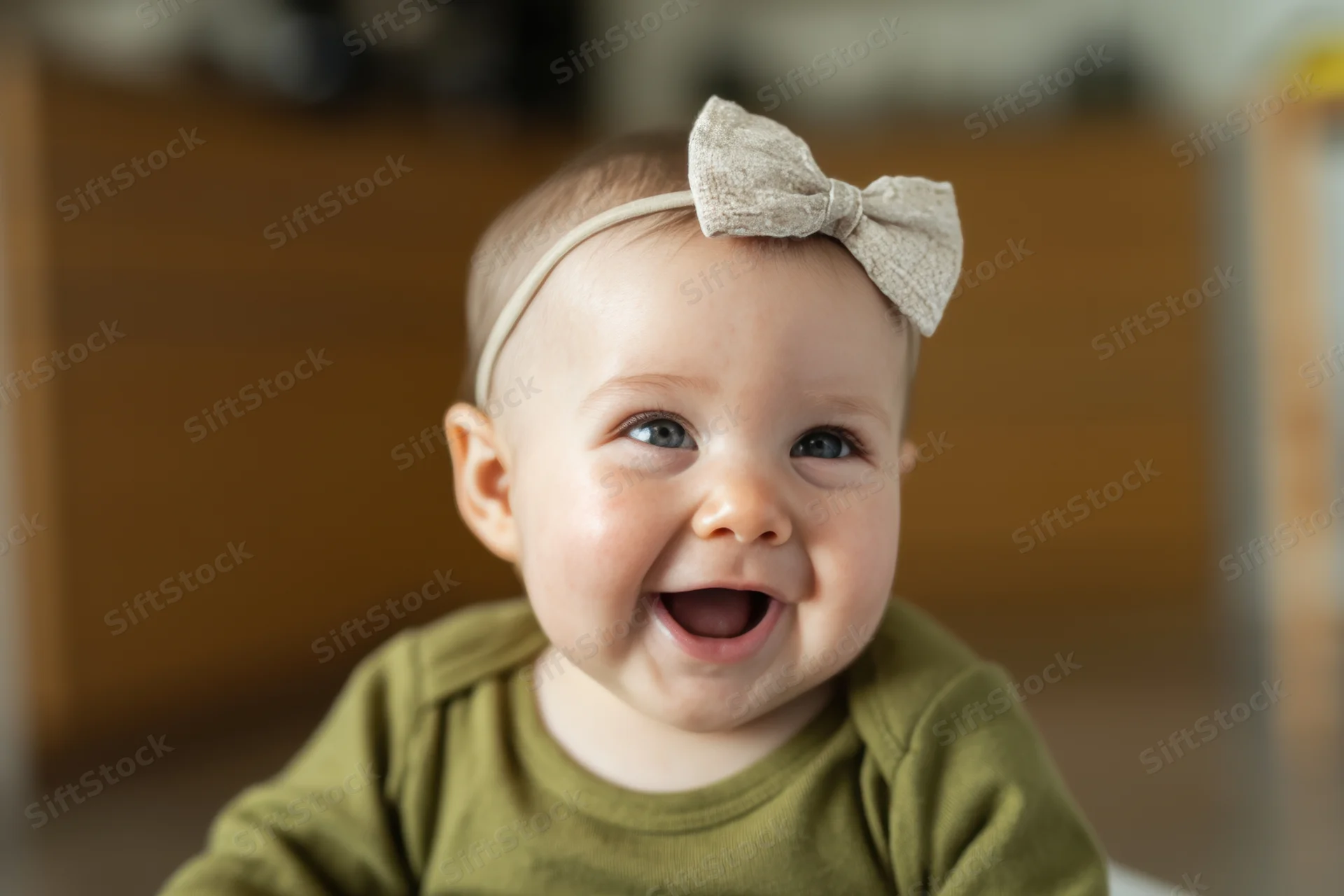 Smiling baby wearing olive green shirt and beige bow headband indoors