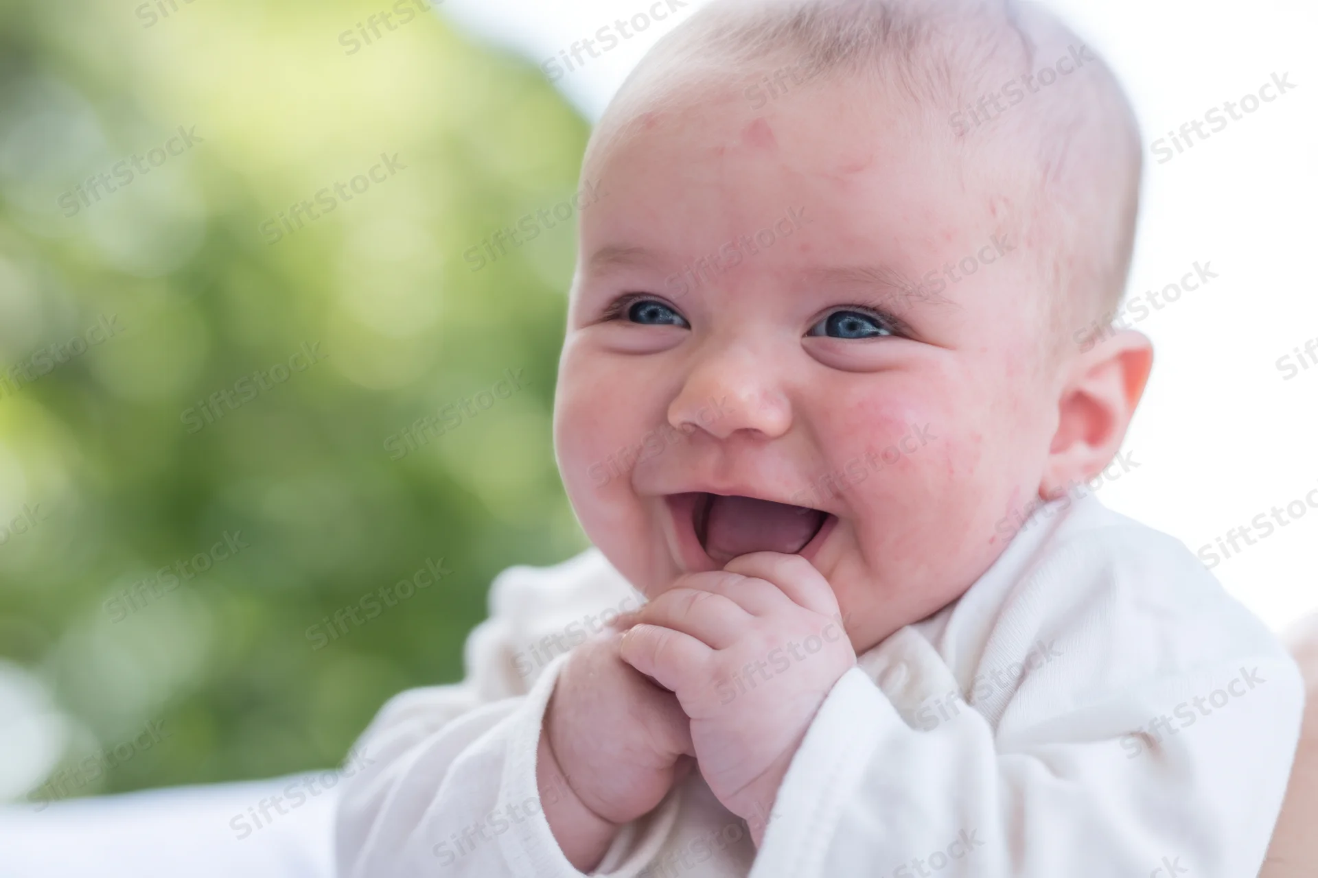 Smiling baby with blue eyes and rosy cheeks outdoors in white clothing