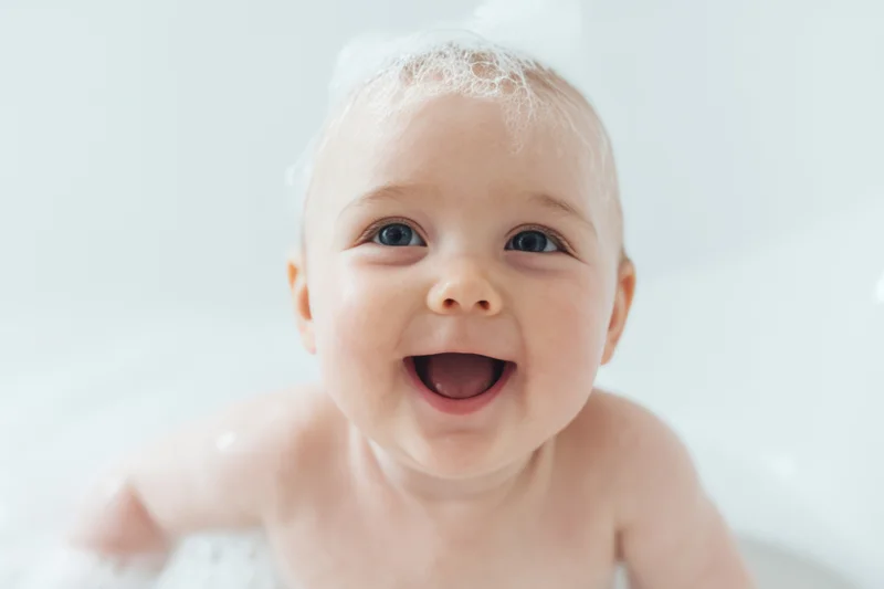 Smiling baby with bubbles on head enjoying bath in tub