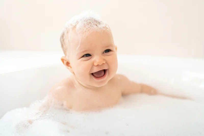 Smiling baby laughing in a bubble bath with foam on its head