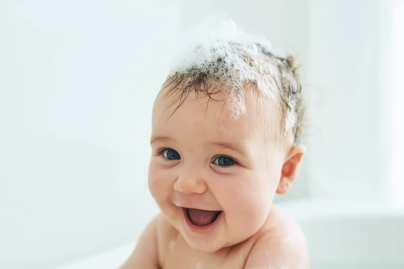 Smiling baby with bubbles on head during bath time