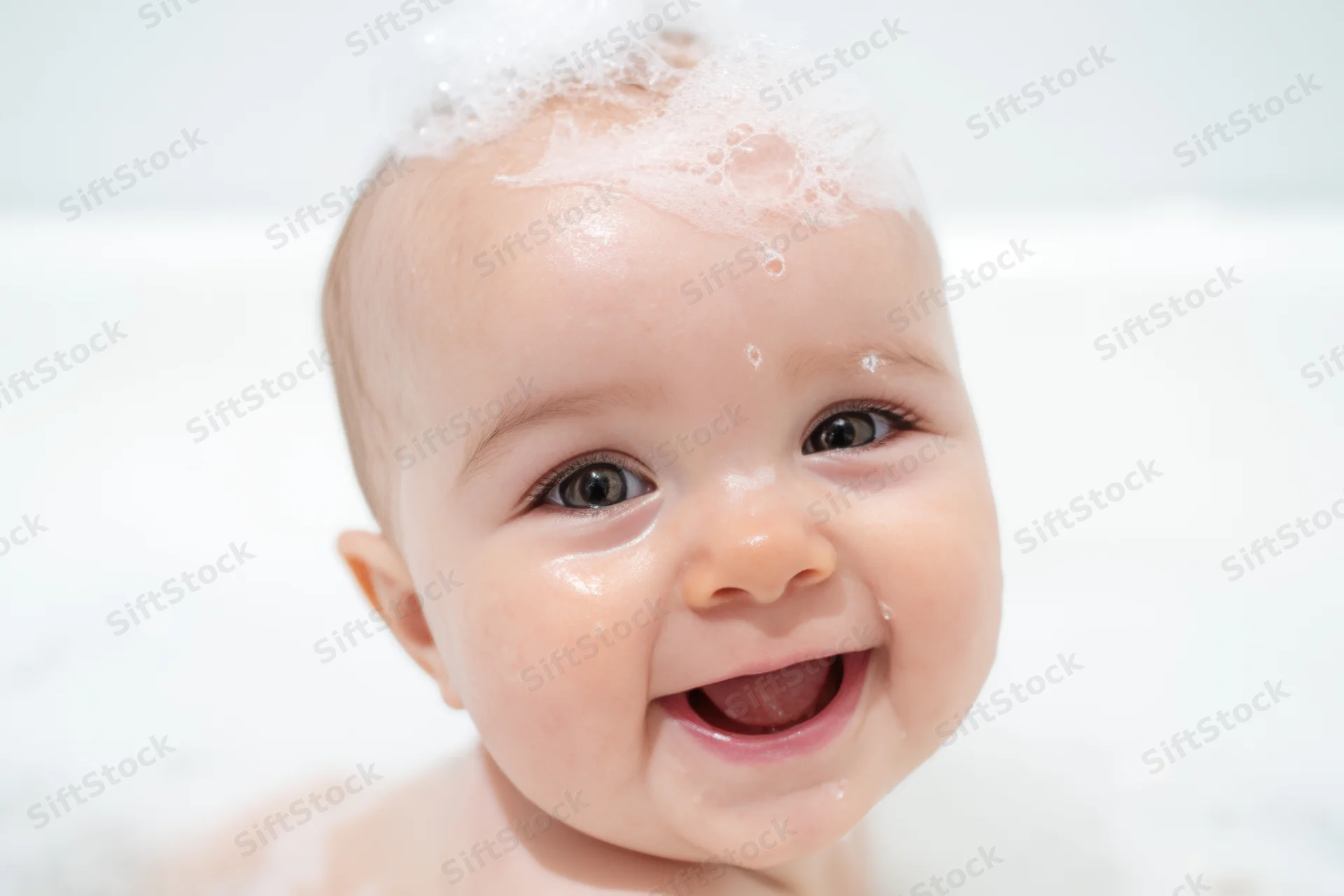 Smiling baby with bubbles on head during bath time