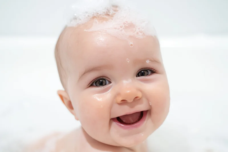 Smiling baby with bubbles on head during bath time
