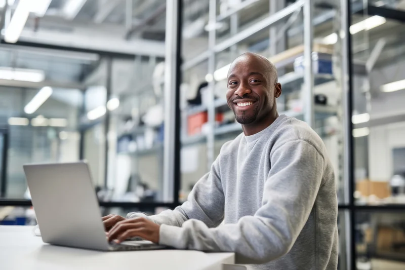 Smiling bald man in gray sweatshirt typing on laptop in modern office workspace