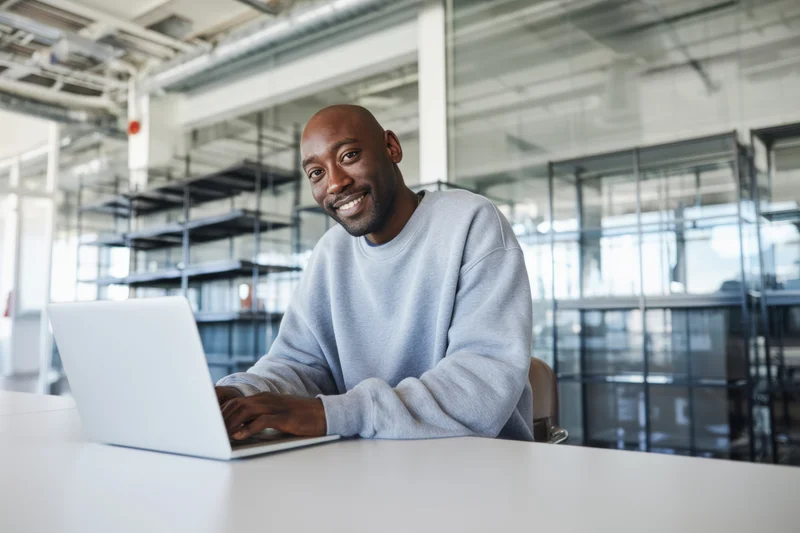 Bald man in gray sweatshirt typing on laptop at office desk smiling