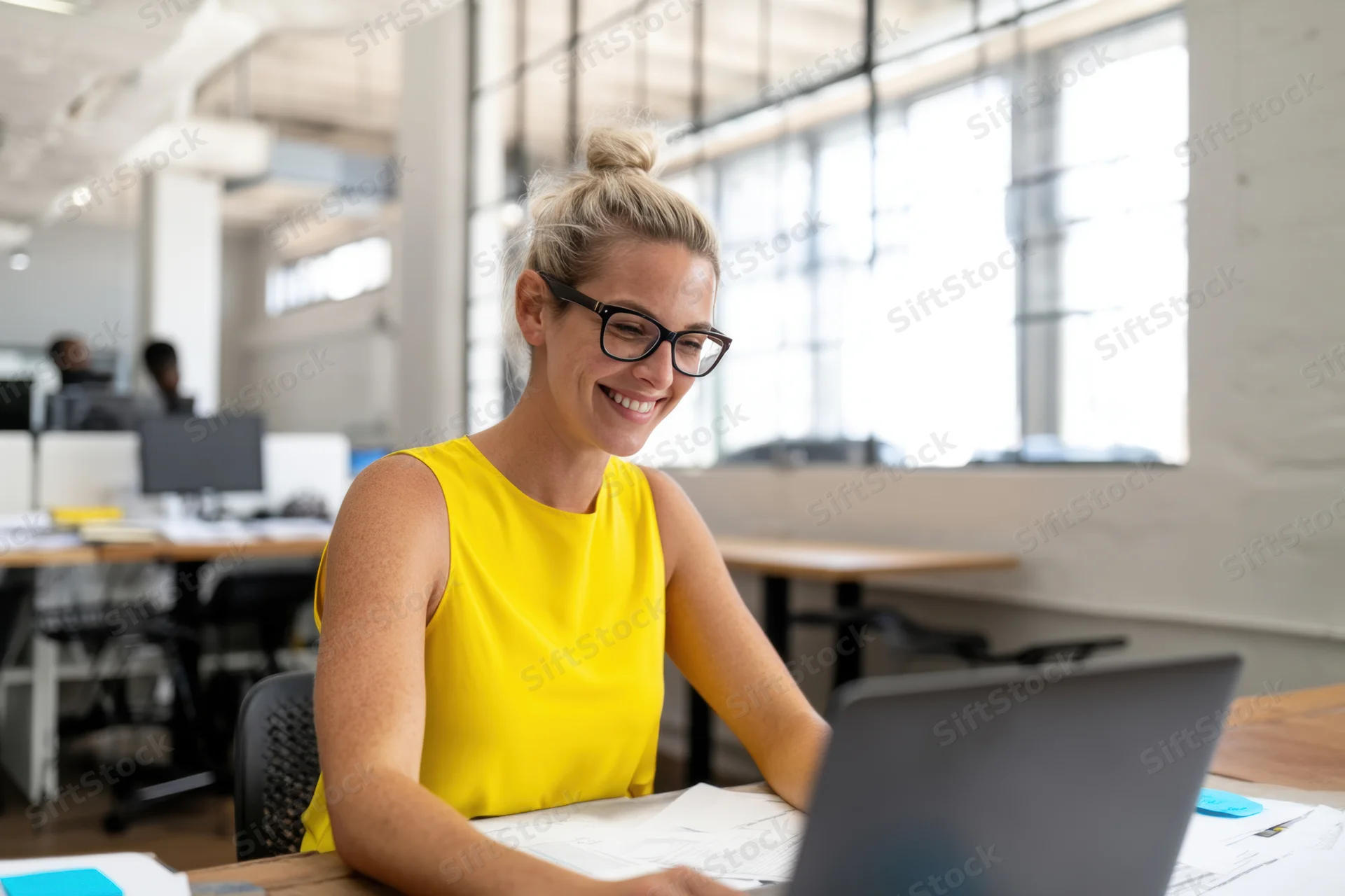 Smiling woman in yellow top using laptop at office desk
