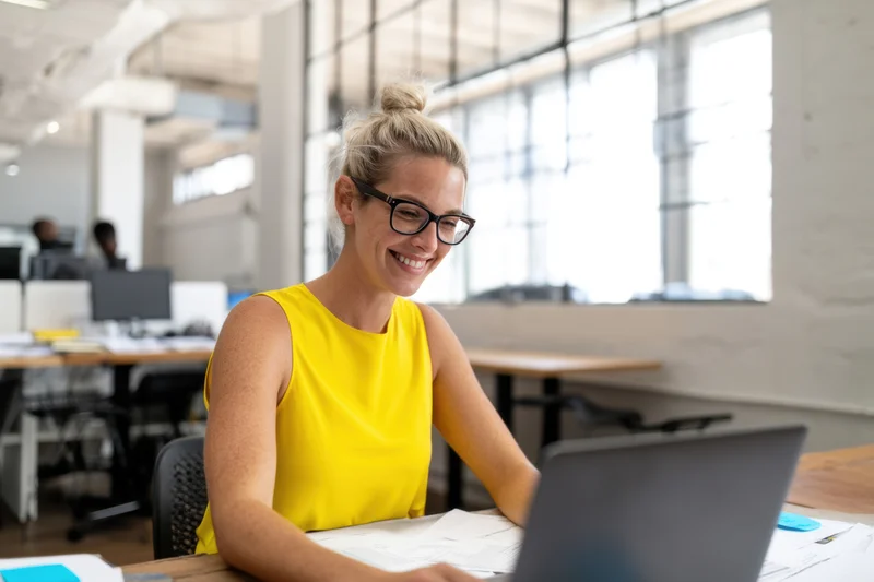 Smiling woman in yellow top using laptop at office desk