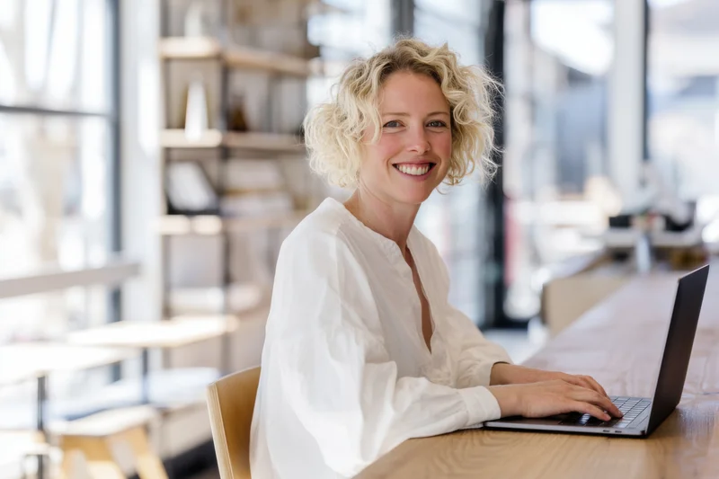Smiling woman typing on laptop at wooden desk in modern office workspace