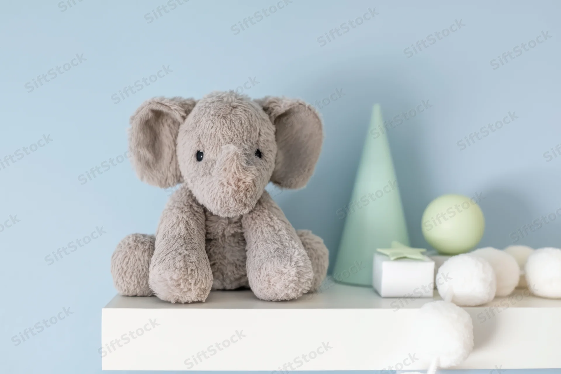 Soft gray plush elephant sitting on white shelf beside pastel decor items