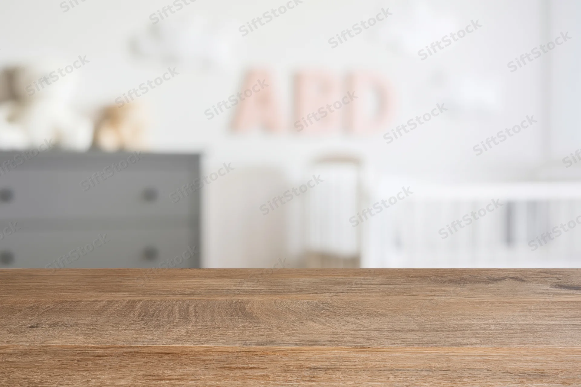Wooden surface in foreground with blurred nursery room behind featuring crib and dresser