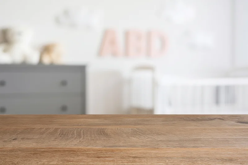Wooden surface in foreground with blurred nursery room behind featuring crib and dresser