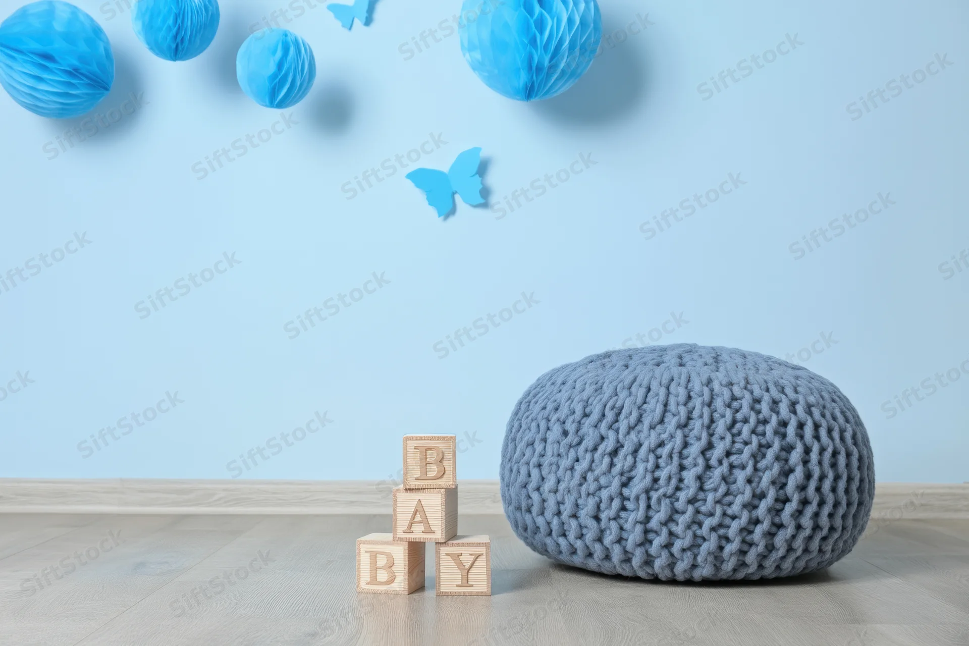 Wooden blocks spelling baby stacked beside a knit pouf in a blue nursery room