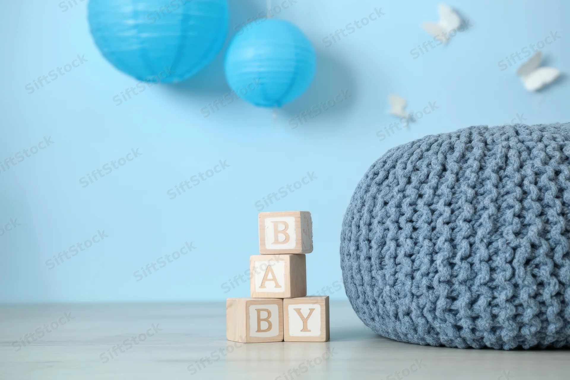 Stacked wooden blocks spelling baby in a blue nursery with crocheted pouf and hanging lanterns
