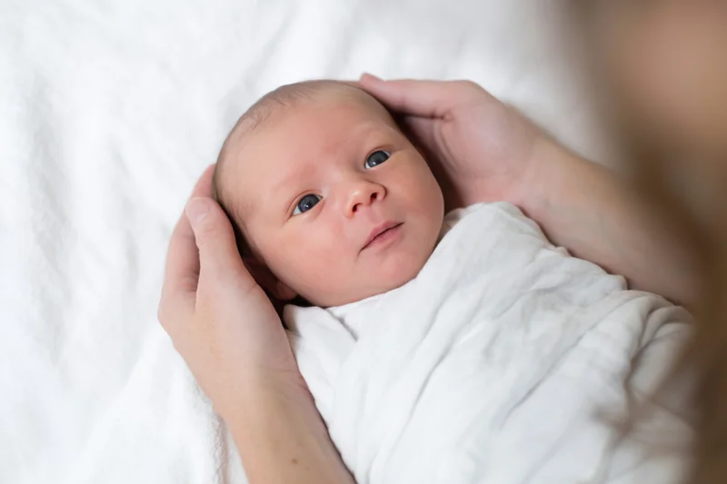 Newborn baby swaddled in white blanket cradled by hands in close-up view