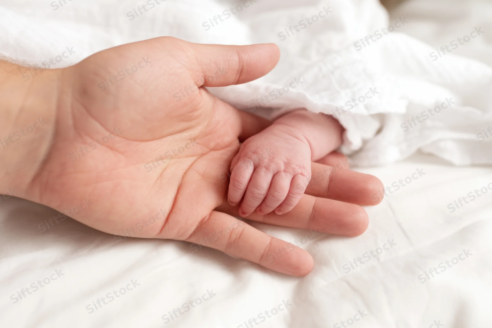 Parent's hand cradling a newborn baby's tiny hand on a white blanket