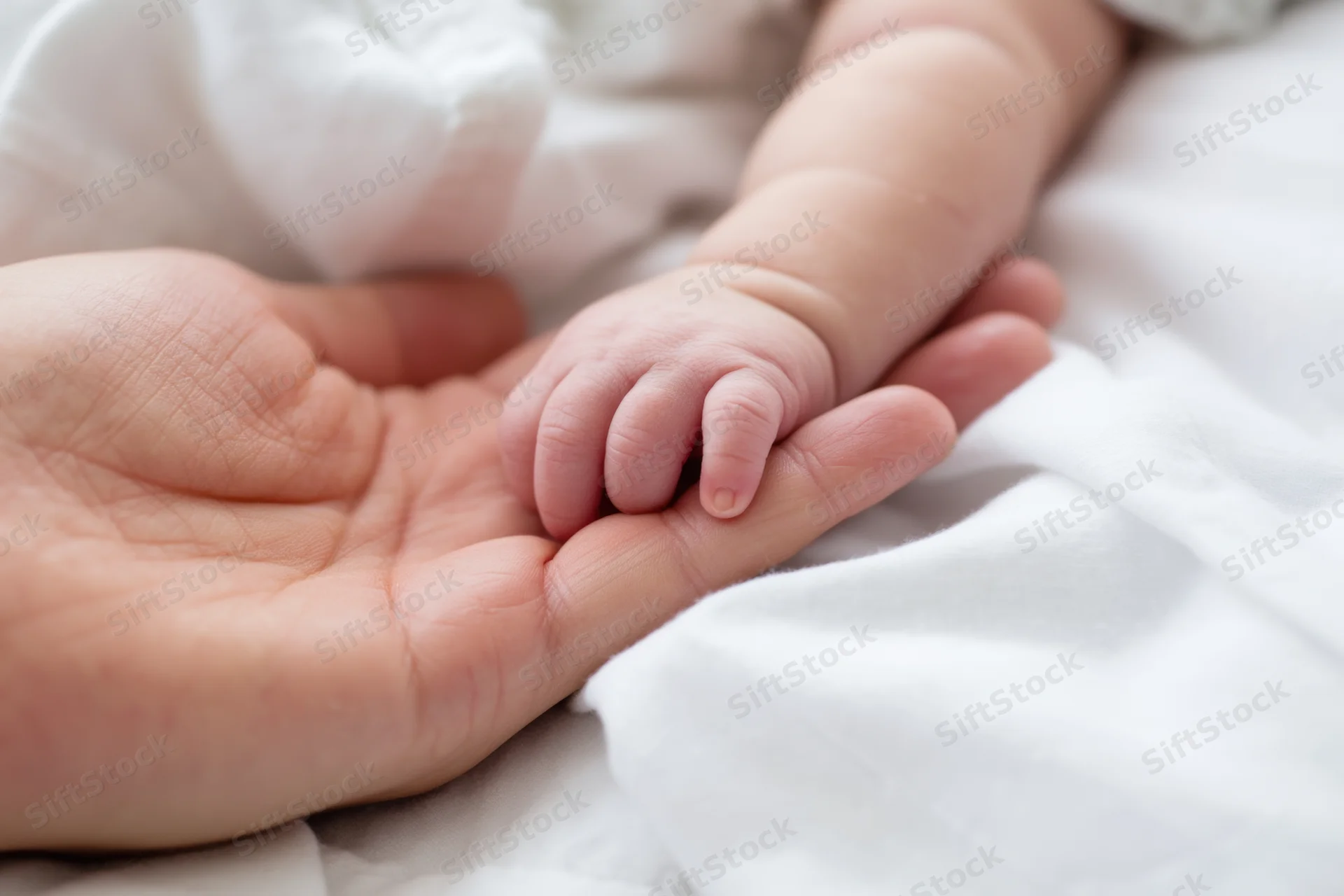 Baby's tiny hand resting on parent's palm on a white blanket