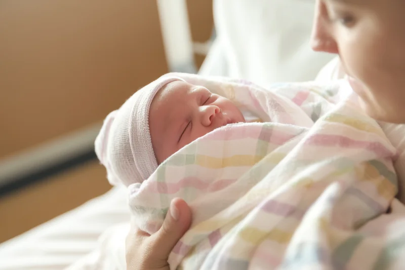 Mother holding swaddled newborn in hospital room