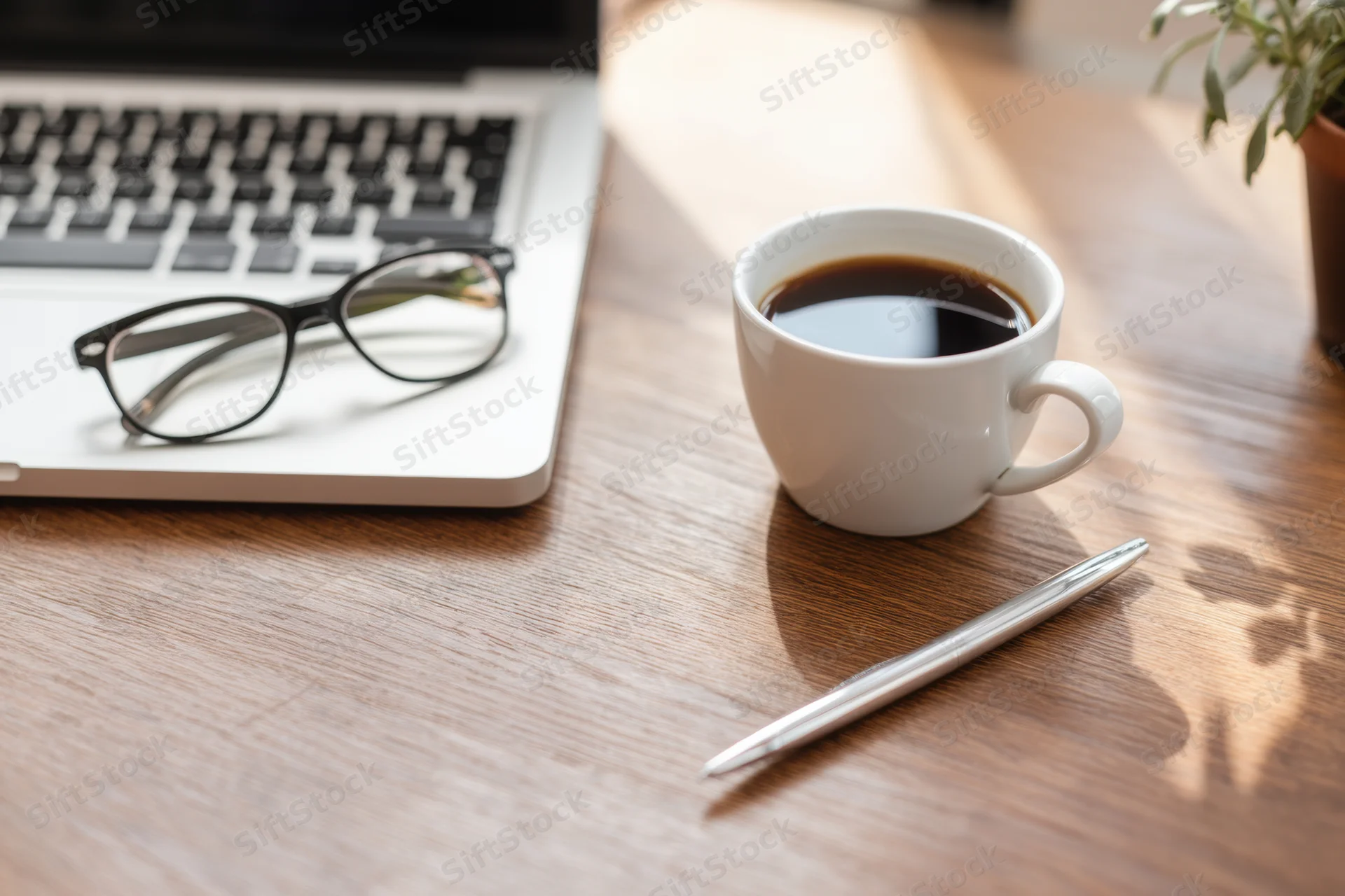 Silver laptop with coffee cup and pen on wooden desk in tidy workspace