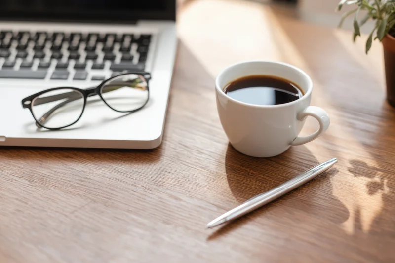 Silver laptop with coffee cup and pen on wooden desk in tidy workspace
