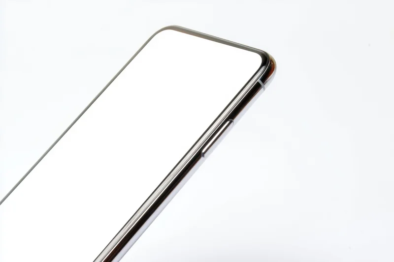 Tilted smartphone with blank white screen and metallic frame showing curved edge and side buttons against white background