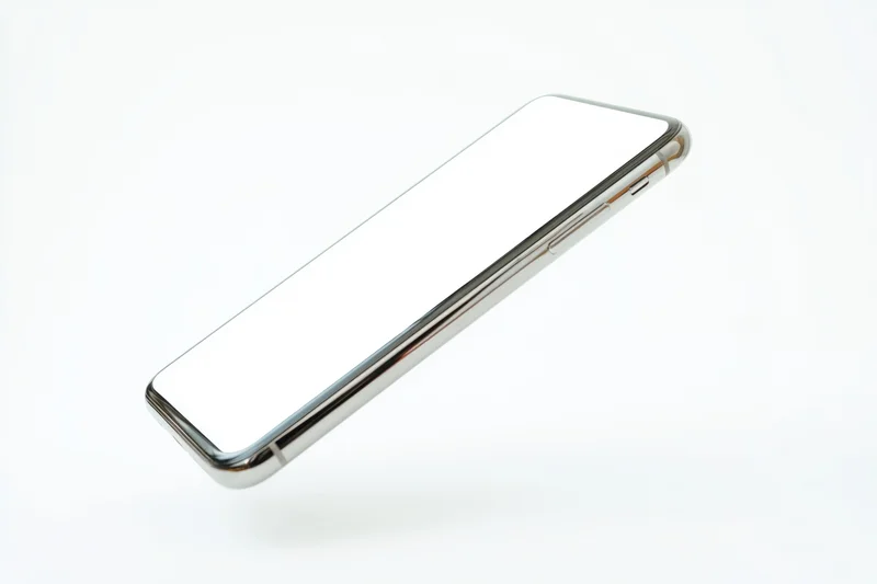 Tilted smartphone with blank white screen and metallic frame floating against white background