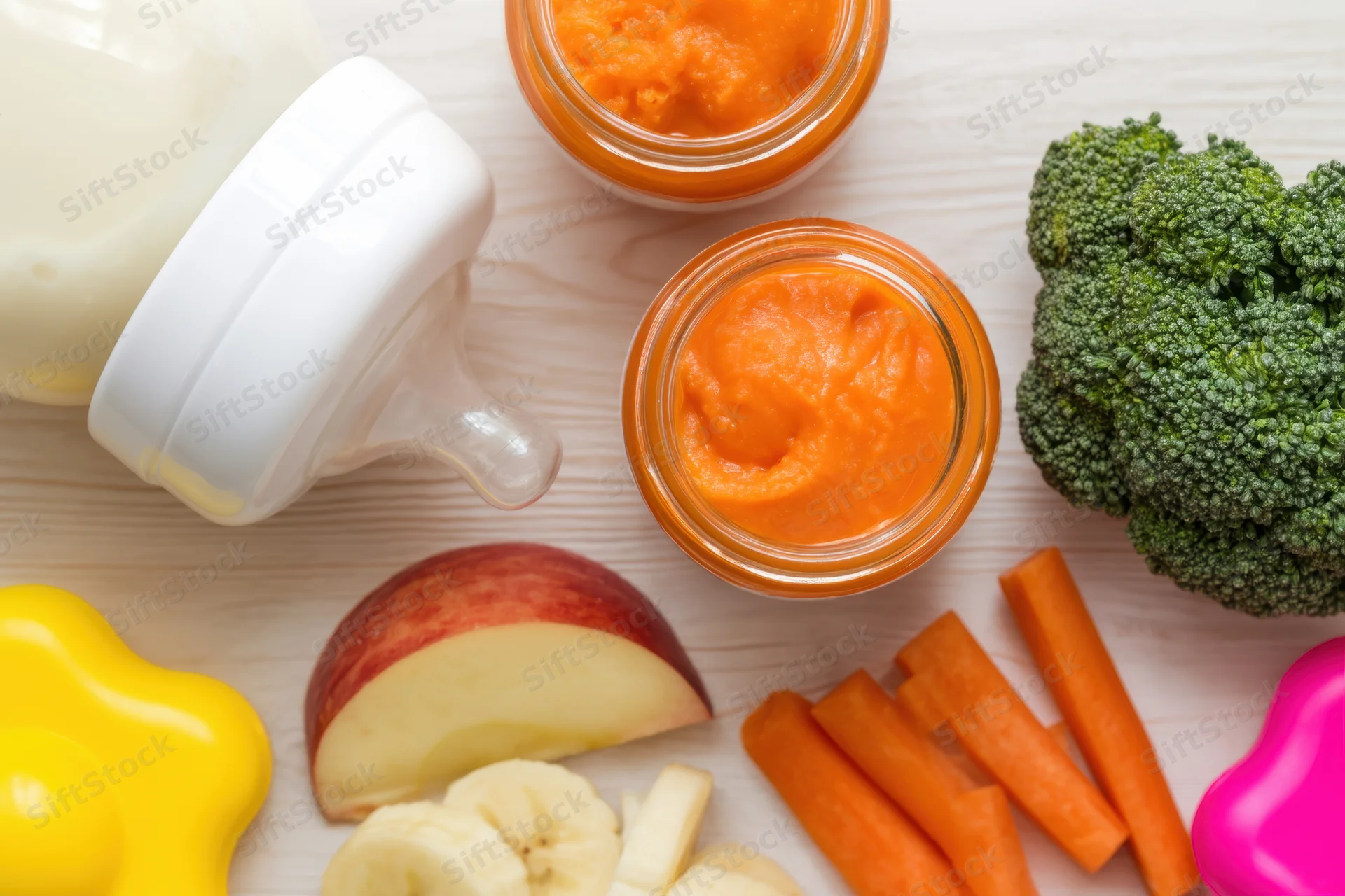 Baby feeding setup with jars of pureed vegetables and fruits on wooden surface