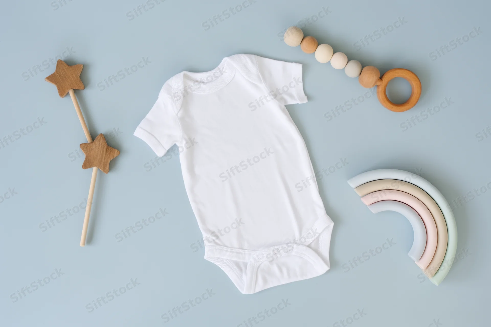 White baby onesie laid flat on soft blue background with wooden toys and rainbow decor