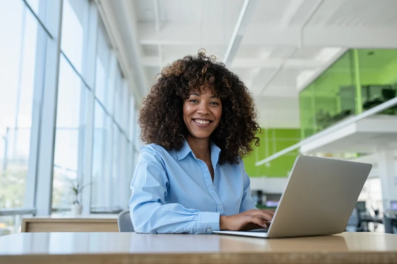 Woman smiling at laptop on wooden desk in bright open office