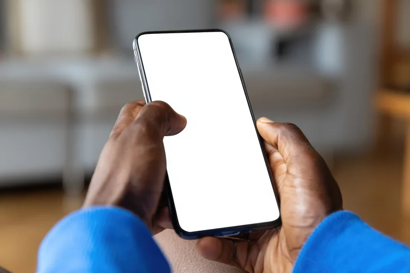 Hands holding smartphone with blank white screen indoors