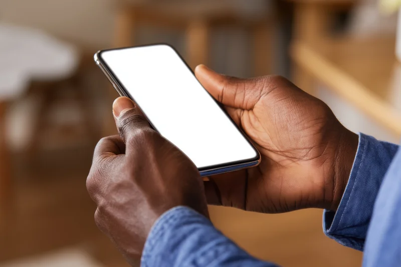 Close-up of hands holding a smartphone with a blank white screen indoors