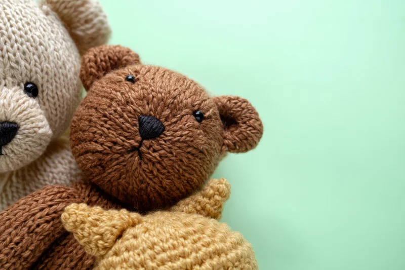 Close up of knitted teddy bears in brown and beige tones arranged together against a mint green background