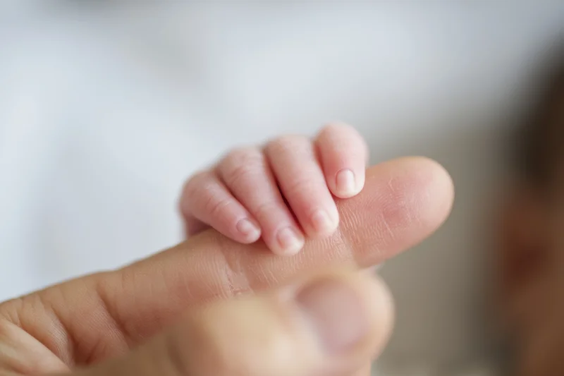 Baby's tiny hand gripping an adult finger in close-up view