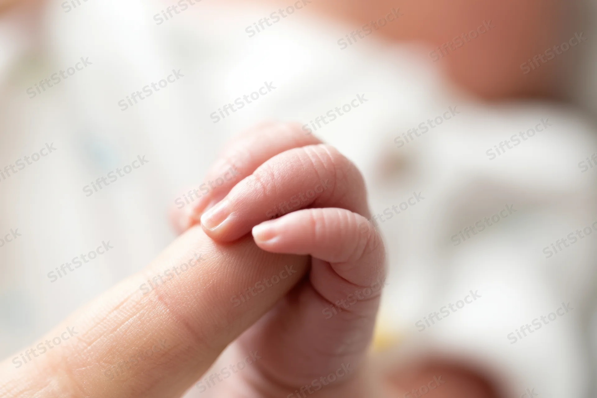 Baby's tiny hand gripping an adult finger in a close-up view