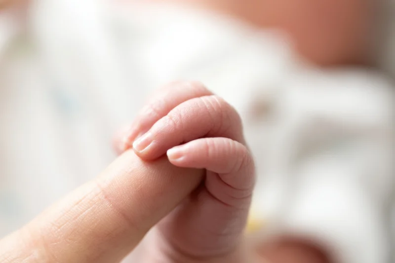 Baby's tiny hand gripping an adult finger in a close-up view