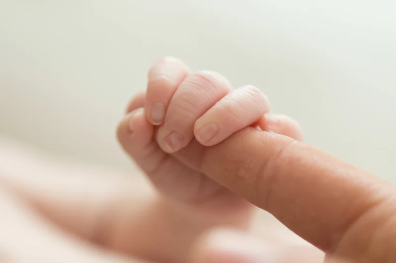 Baby's tiny hand gripping an adult finger in close-up view