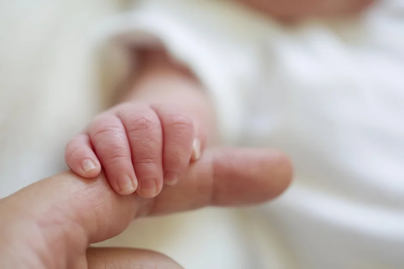 Baby's tiny hand gripping an adult finger in close-up view