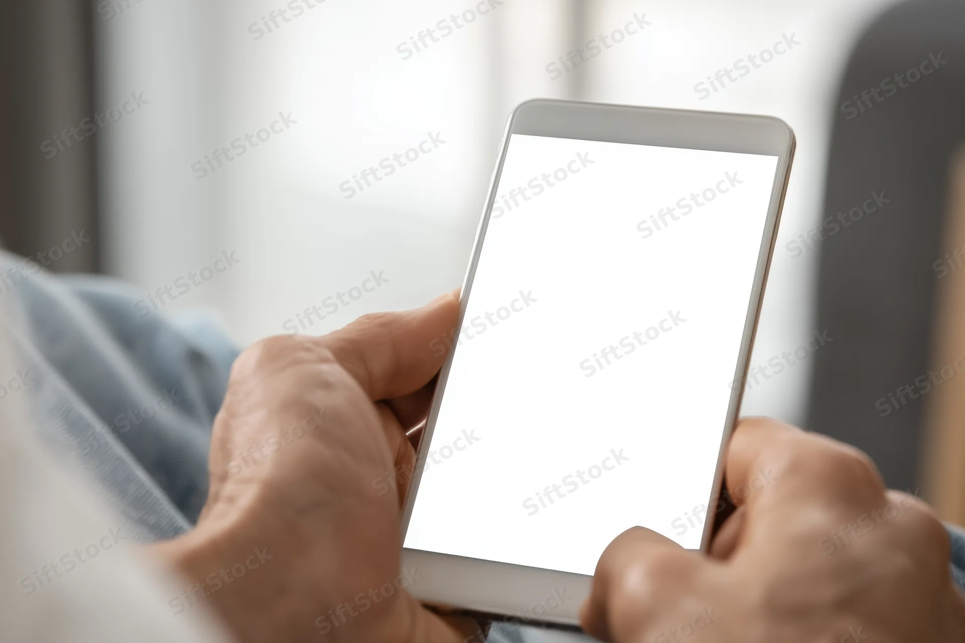 Closeup of elderly hands holding a smartphone with a blank white screen indoors