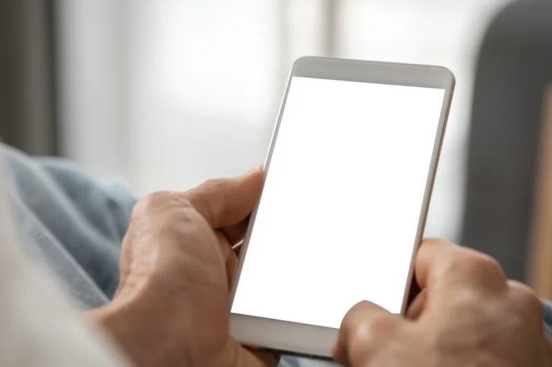 Closeup of elderly hands holding a smartphone with a blank white screen indoors