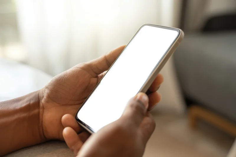 Hands holding a smartphone with a blank white screen indoors
